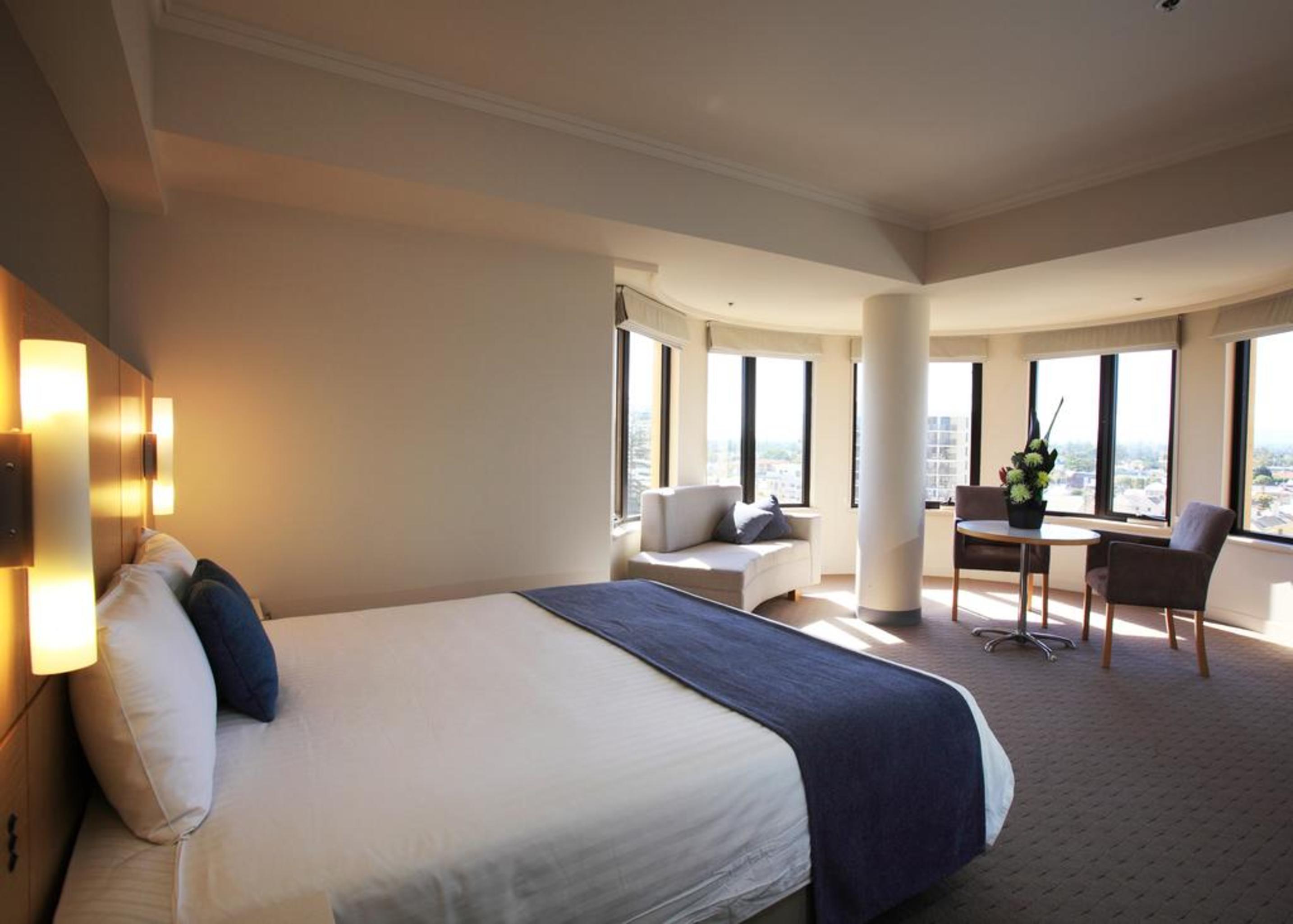 Hotel Stamford Grand Adelaide Glenelg Exterior foto The photo shows a hotel room with a modern and spacious design. There is a large bed with white linens and a dark blue throw blanket. The room features multiple windows that allow plenty of natural light, and there is a small seating area near the wi