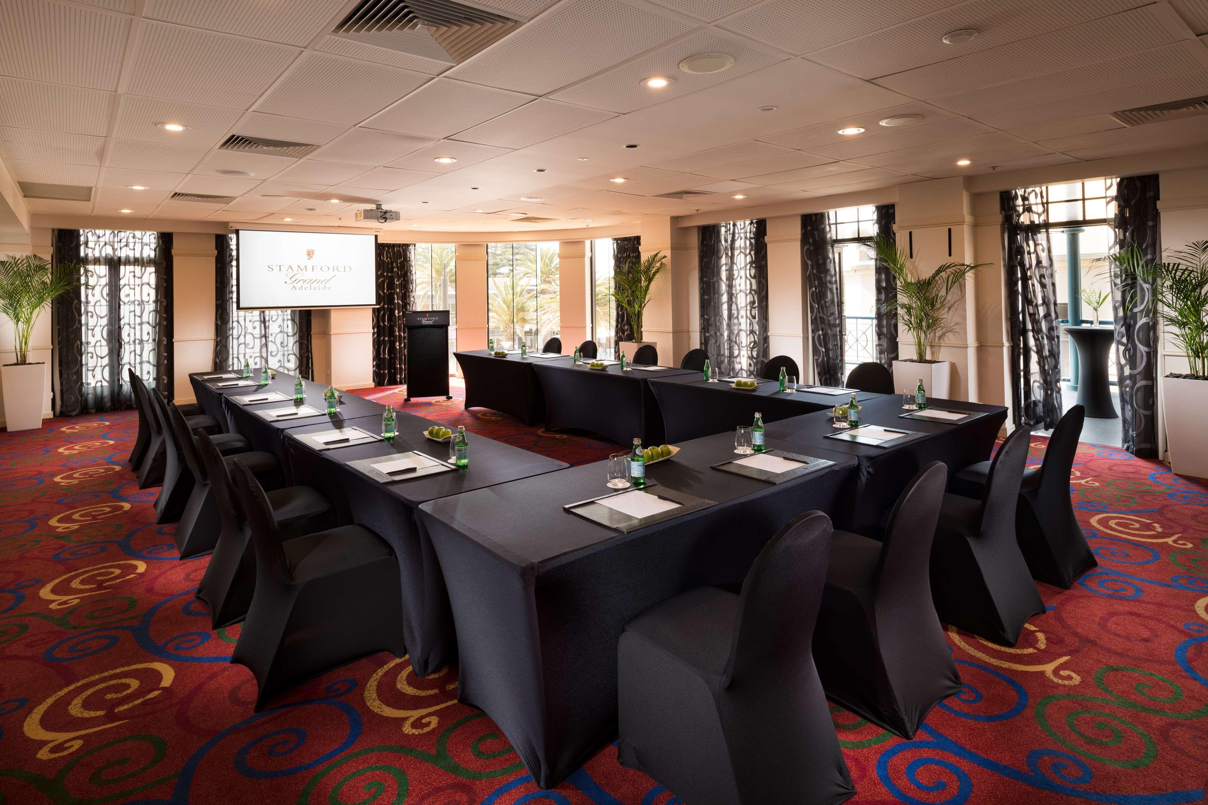 Hotel Stamford Grand Adelaide Glenelg Exterior foto The photo shows a conference room set up for a meeting or presentation. There are several tables arranged in a U-shape, covered with black tablecloths. Each table has a notepad and a small bottle of water on it. The chairs around the tables are also 