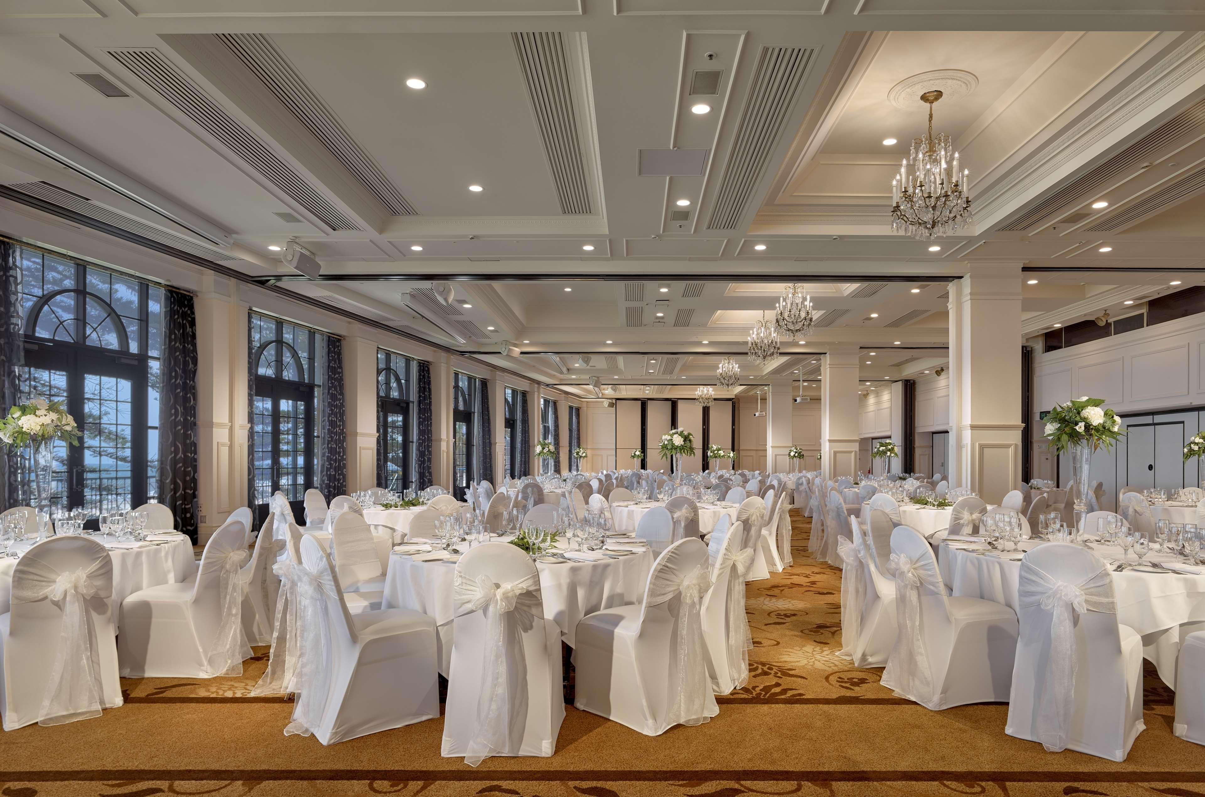 Hotel Stamford Grand Adelaide Glenelg Exterior foto The photo depicts an elegantly arranged banquet hall or dining area. The space features multiple round tables, each set with white tablecloths and decorated with floral centerpieces. The chairs are covered in white fabric, contributing to a formal at