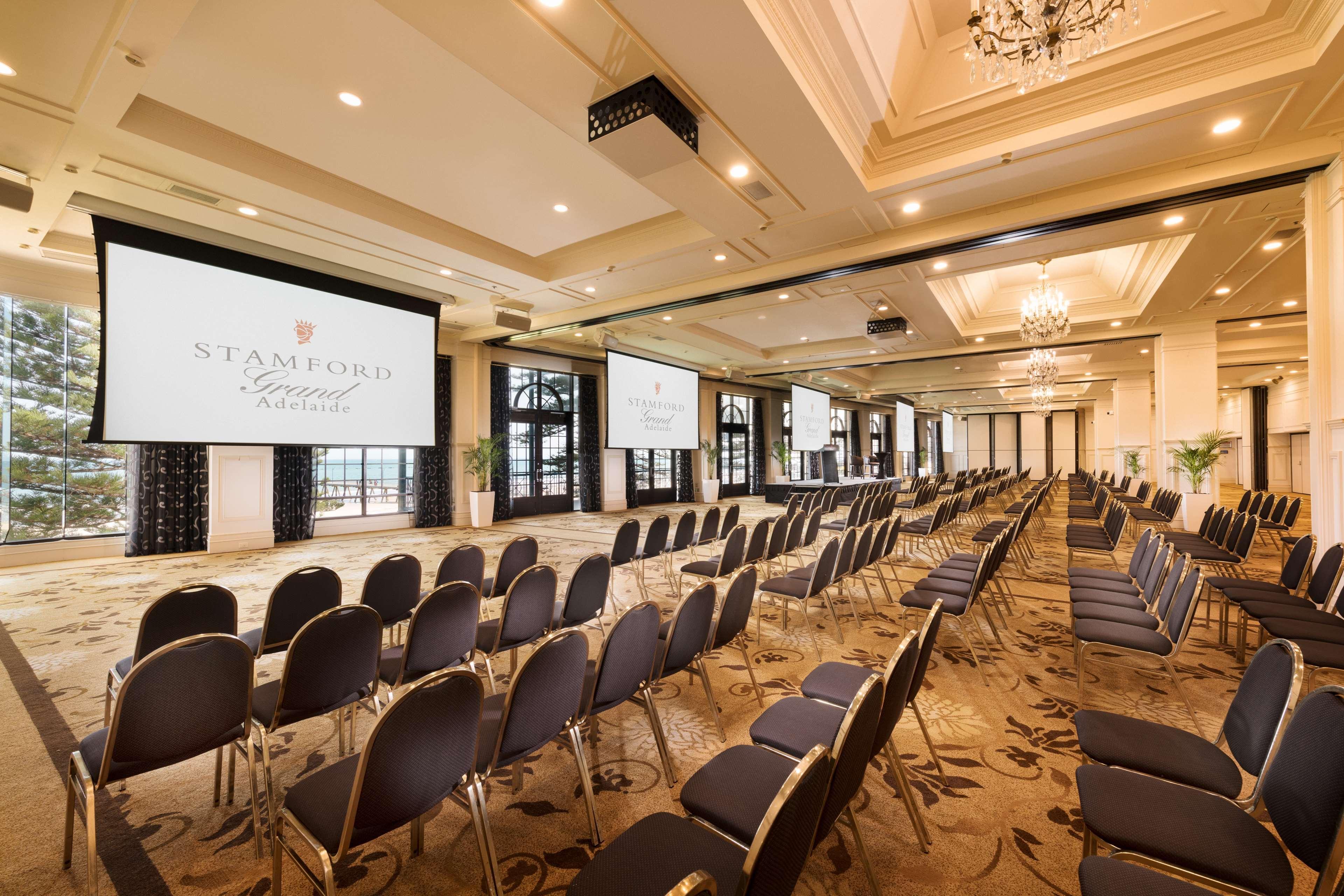 Hotel Stamford Grand Adelaide Glenelg Exterior foto The photo shows a spacious event or conference room. There are rows of dark, upholstered chairs arranged facing two large screens. The room features elegant decor with soft lighting, a chandelier, and windows that allow natural light to filter in. Th