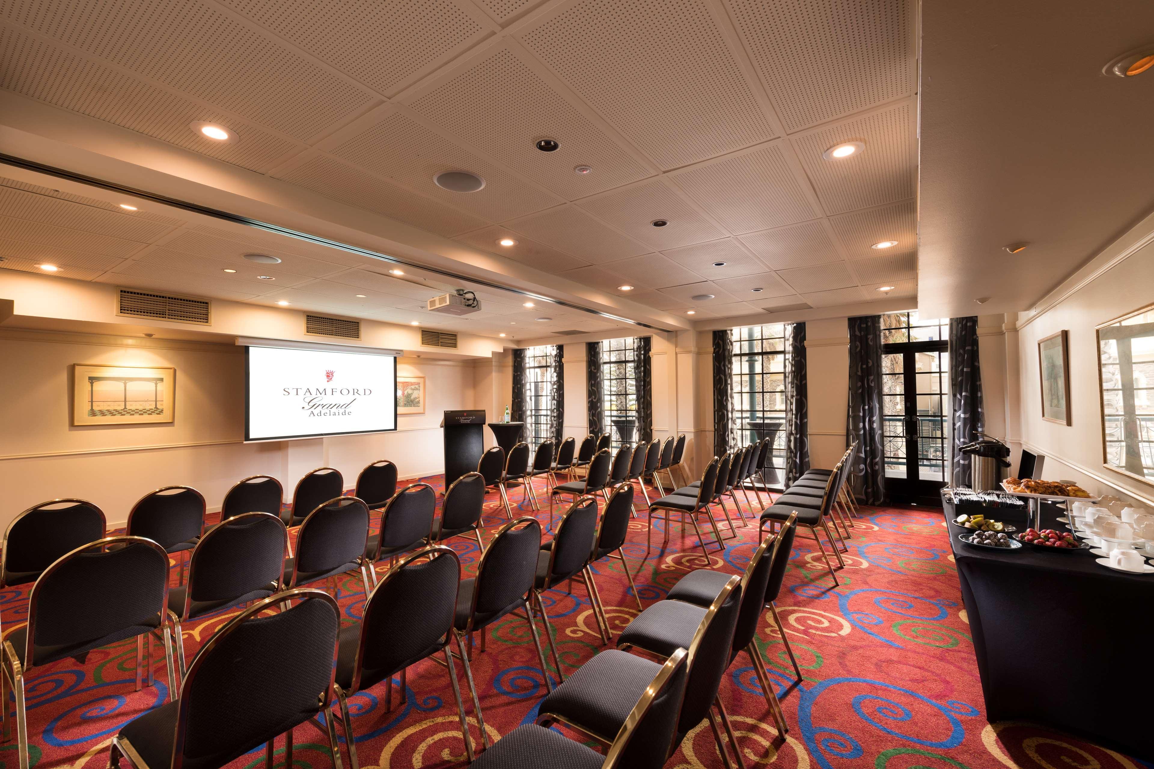 Hotel Stamford Grand Adelaide Glenelg Exterior foto The photo shows a conference room set up for an event. There are rows of black chairs arranged in a semicircular formation facing a presentation screen at the front. The room features large windows that allow natural light to enter, and the flooring 