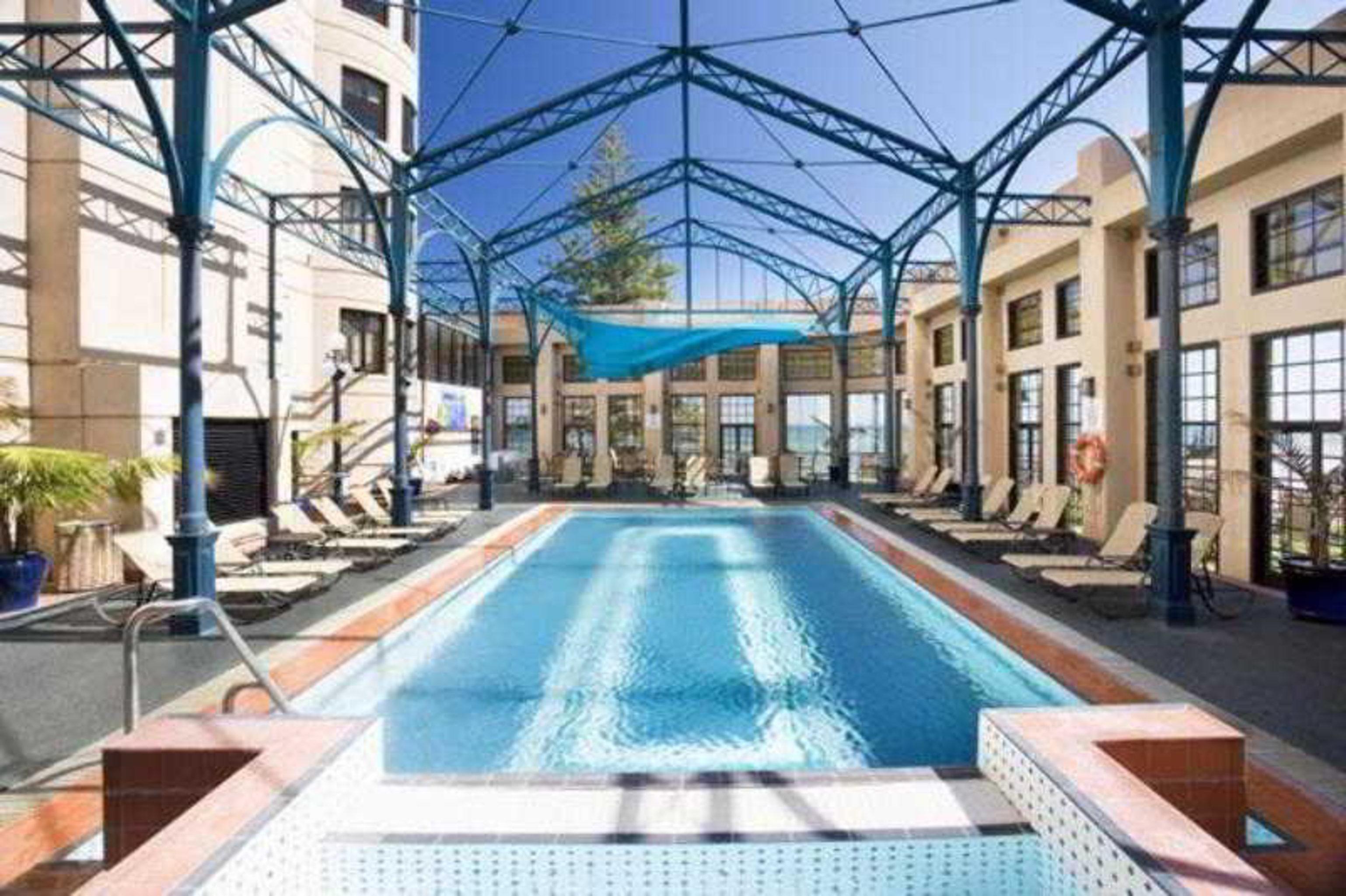 Hotel Stamford Grand Adelaide Glenelg Facilidades foto The photo shows an indoor swimming pool area. The pool is rectangular and features a blue cover above, supported by a metal frame. Surrounding the pool are several lounge chairs, and the space is well-lit with large windows allowing natural light to 
