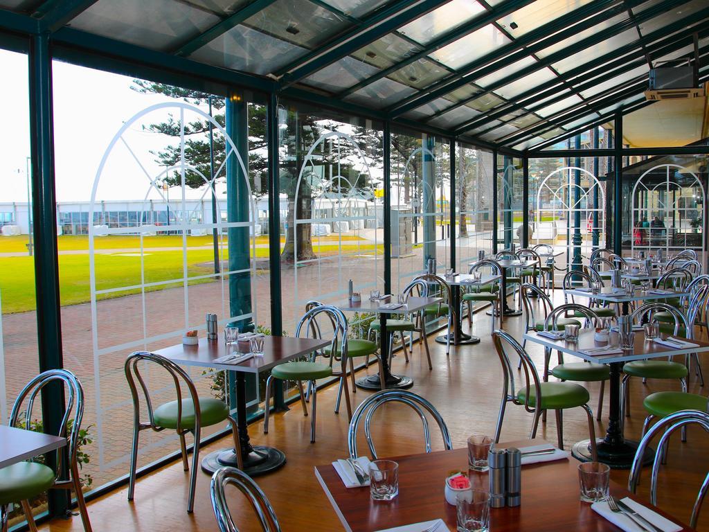 Hotel Stamford Grand Adelaide Glenelg Exterior foto The photo shows the interior of a restaurant with a modern design. The space features several tables with green chairs, arranged in a way that allows for ample seating. Large glass windows provide a view of the outside, creating a bright and open atm